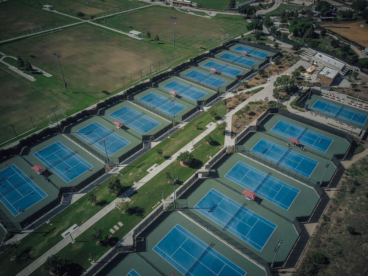 Vue aérienne d’un complexe sportif comptant une quinzaine de courts de tennis et plusieurs terrains en herbe.